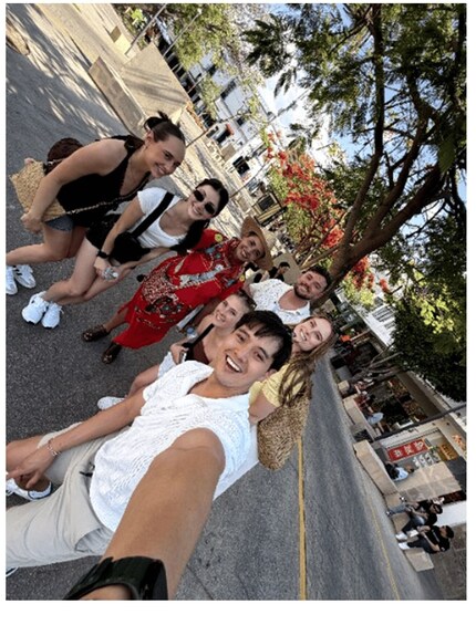 A group of people taking a selfie on a street with trees and buildings in the background. 1
