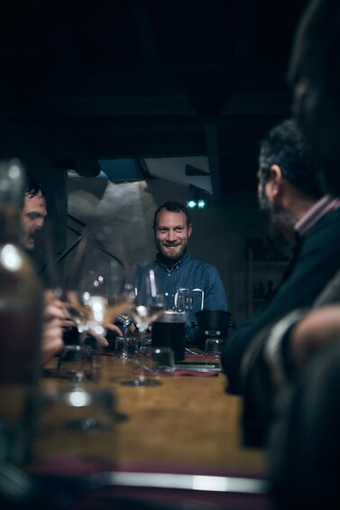A group of people seated around a table with glasses of wine, in a dimly lit indoor setting. 1