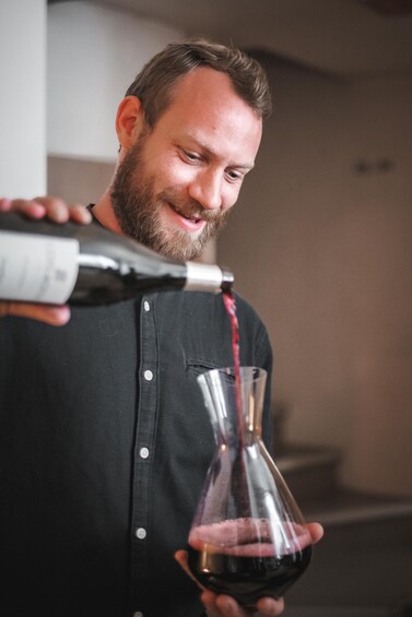 A person pouring red wine from a bottle into a glass. 3