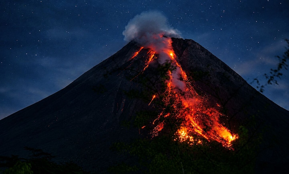 Un volcán en erupción nocturna con lava descendiendo por su flanco. 5