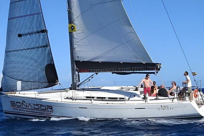 A sailboat with people on deck, a clear sky, and calm water. 4