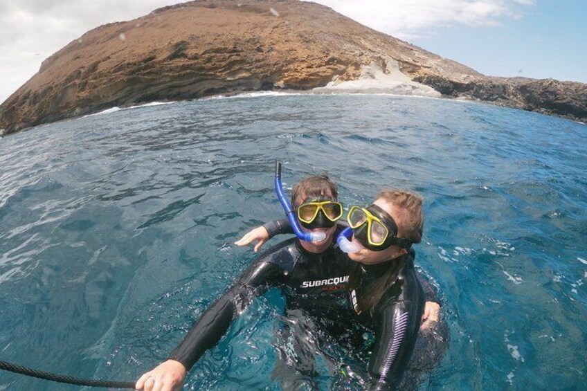 Two people scuba diving in clear blue water with a rocky coastline in the background. 5