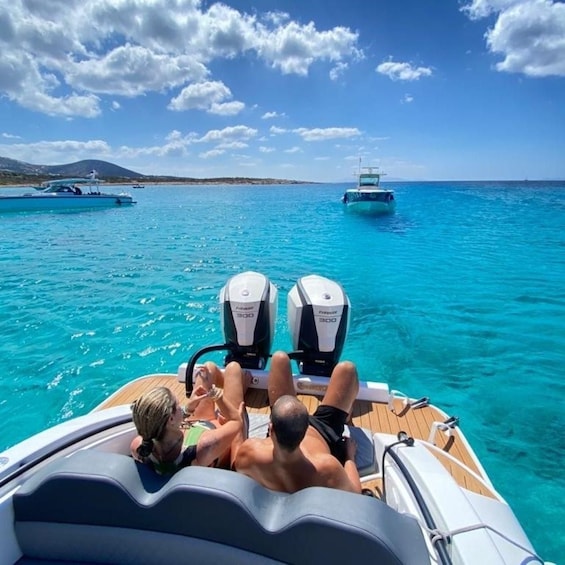 A boat with two outboard motors, passengers relaxing, and another boat in the distance on a clear blue sea. 3