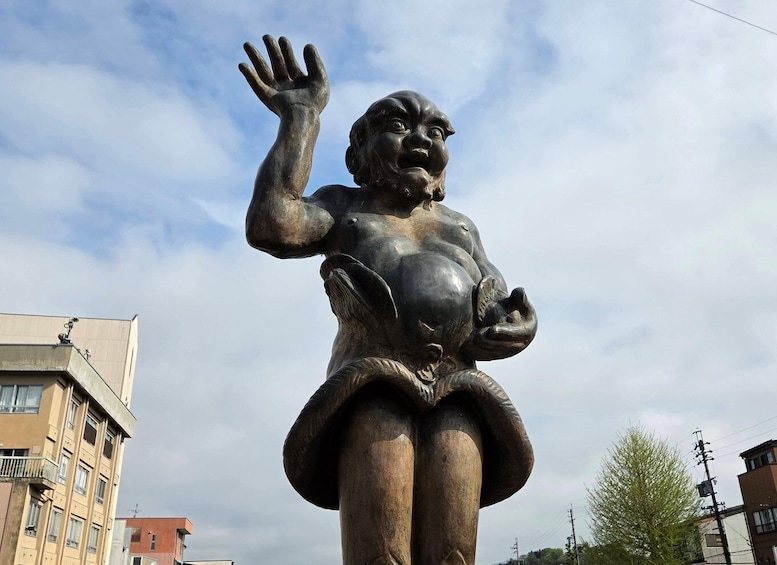 A bronze statue of a woman with raised hand, set against a backdrop of buildings and a cloudy sky. 4