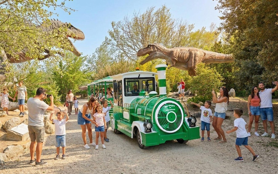 A green and white miniature train with people around it, including a dinosaur model above the train. 1