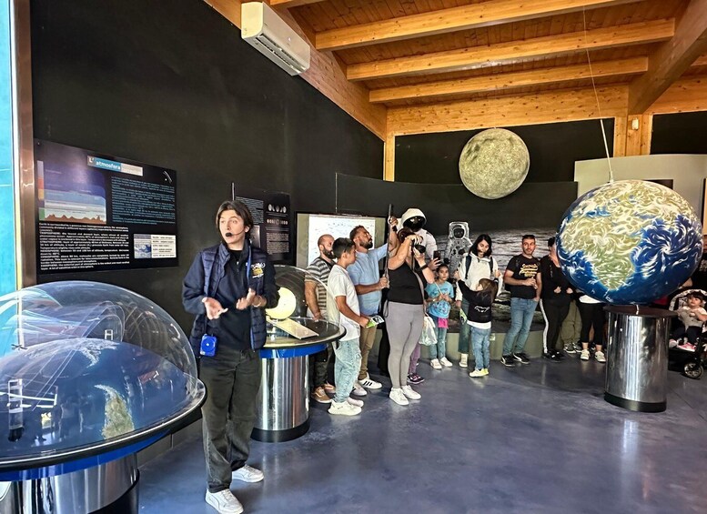 A group of people at a science museum with exhibits including a large globe and a transparent dome. 3