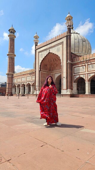 A person in a red dress standing in front of a historic building with arches and a large dome. 4