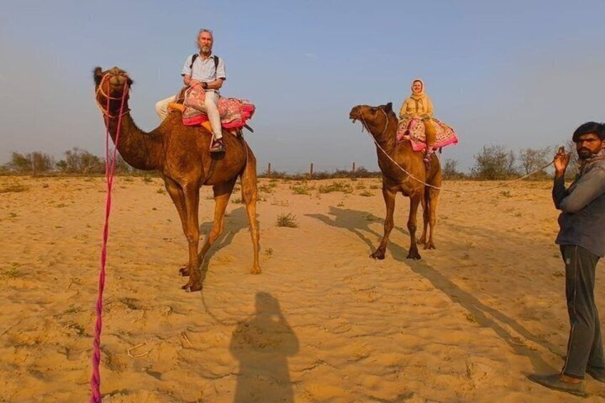 Two camels with riders in a desert landscape. 1