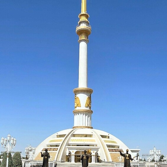 A monument with a tall white column topped with a golden finial, surrounded by statues and a large white dome structure. 2