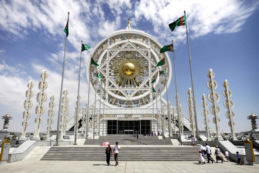 A large, ornate building with a central golden dome, surrounded by flagpoles and steps leading up to the entrance. 1