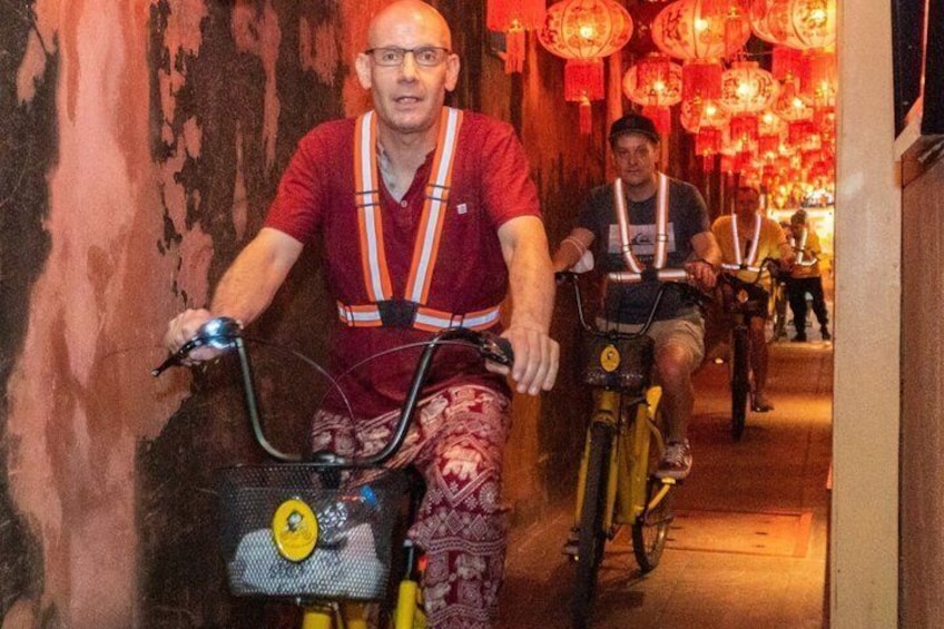 Two people riding bicycles in a corridor with red lanterns. 1