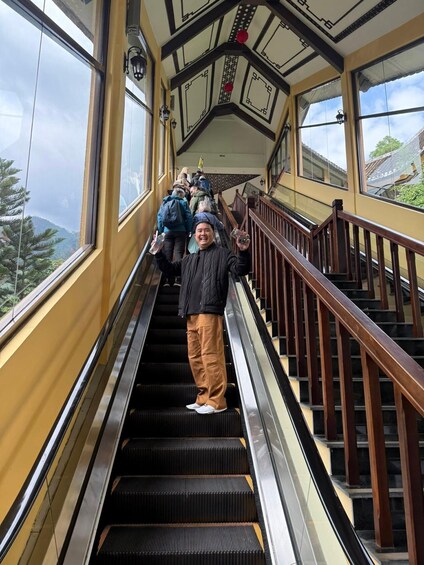 A person on an escalator inside a building with large windows and a wooden railing. 5
