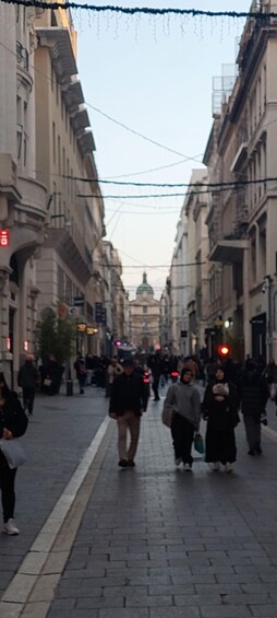 A busy urban street with pedestrians, historic buildings, and a clear sky. 2