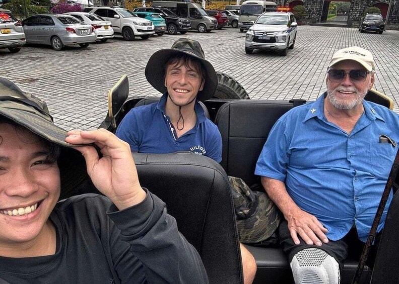 Three people seated in a vehicle with a parking lot in the background. 1