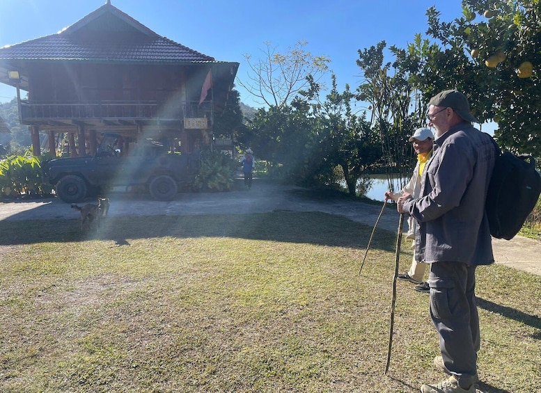 A man with a walking stick near a gazebo, a parked vehicle, and a body of water in the background. 2