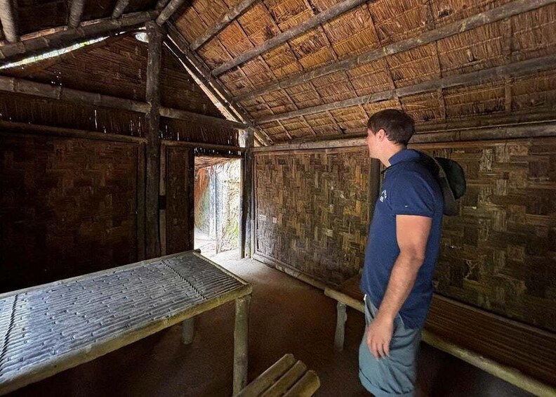 A rustic wooden room with a thatched roof, a bench, and a person standing. 4