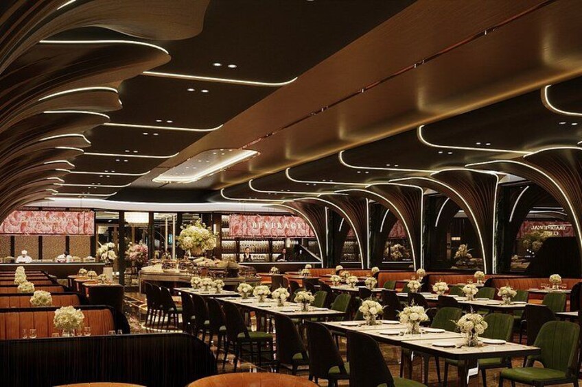 A modern restaurant interior with curved ceiling lights, long tables with white tablecloths, and green chairs. 5