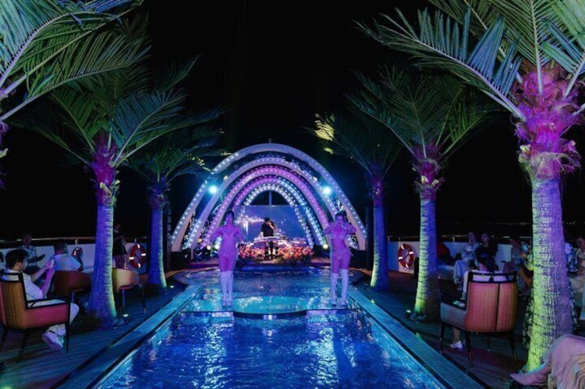 A pool with a stage and palm trees, surrounded by lounge chairs. 4