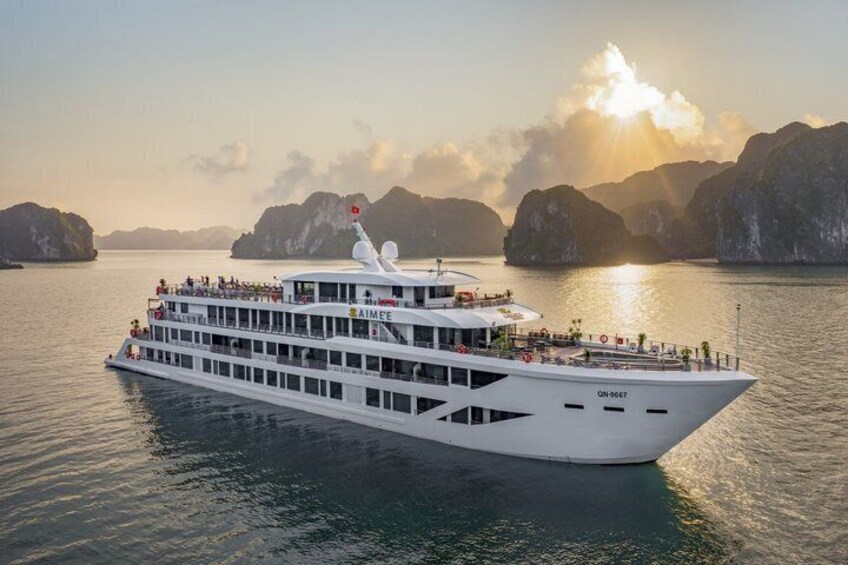 A large white cruise ship with multiple decks and passengers, sailing in a bay with mountainous islands in the background. 1