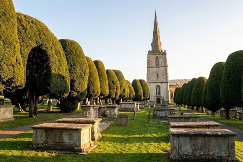 A cemetery with neatly trimmed hedges and a church tower in the background. 4
