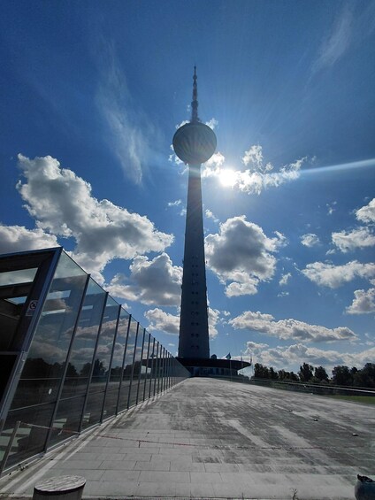 A tall tower with a spherical observation deck, a clear sky with scattered clouds, and a modern glass building to the left. 5