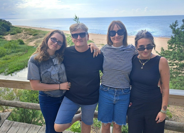 Four people standing on a wooden deck overlooking a beach with a clear view of the ocean. 5