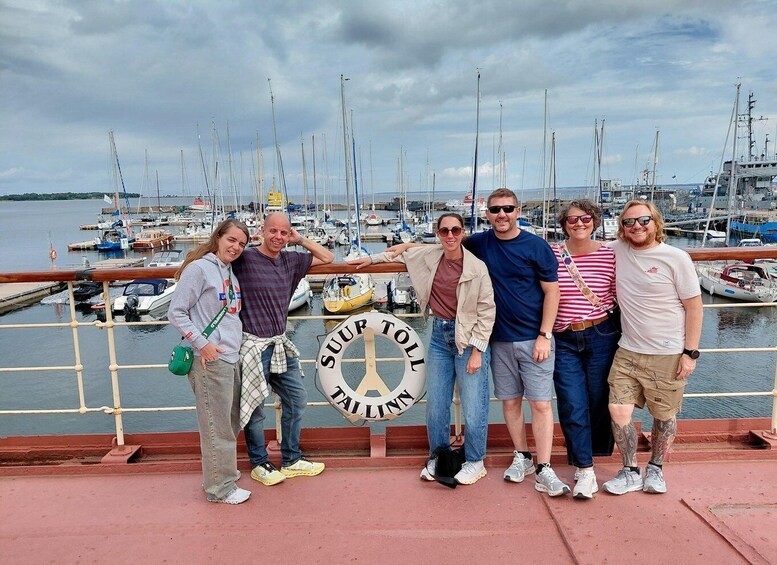 A group of people posing in front of a harbor with sailboats and a lifebuoy. 2