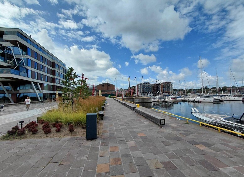 A waterfront promenade with a modern building, marina, and boats. 3