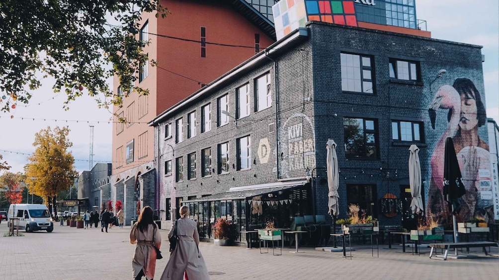 A street with a brick building featuring a large mural, a café with outdoor seating, and pedestrians. 4