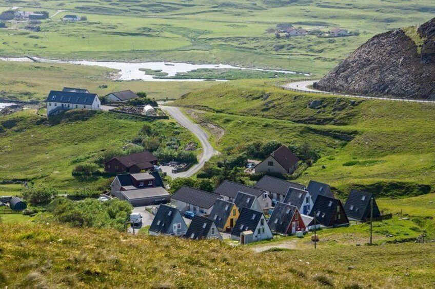 A rural village with houses on a hillside, a winding road, and a large rock formation in the distance. 2