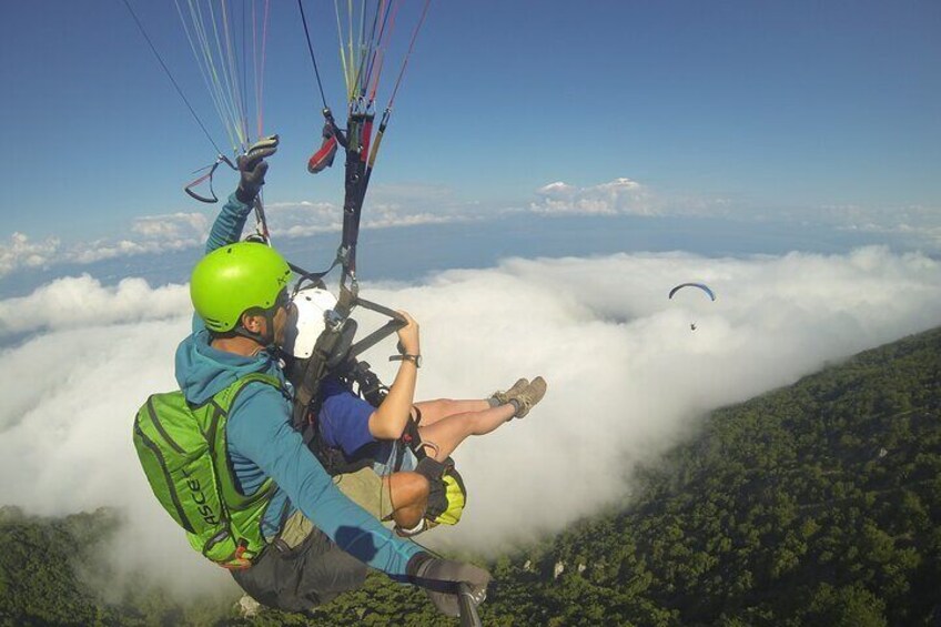 A person paragliding above clouds with a forested mountain below. 1