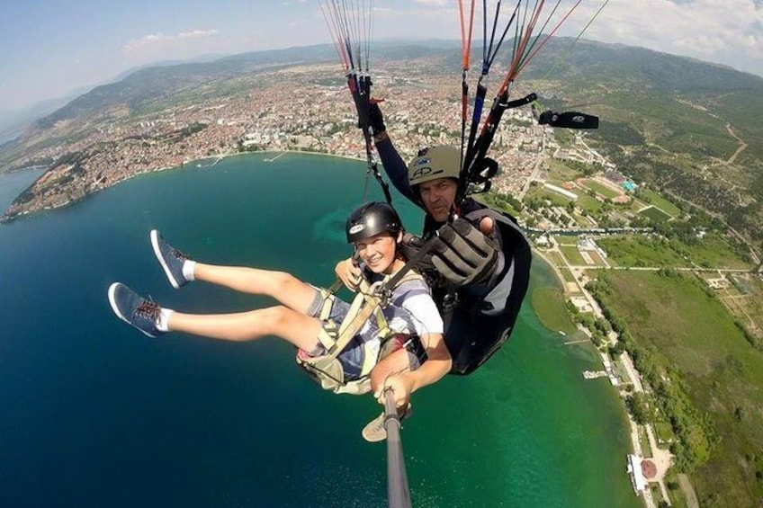 Two people paragliding over a body of water with a coastal town in the background. 1