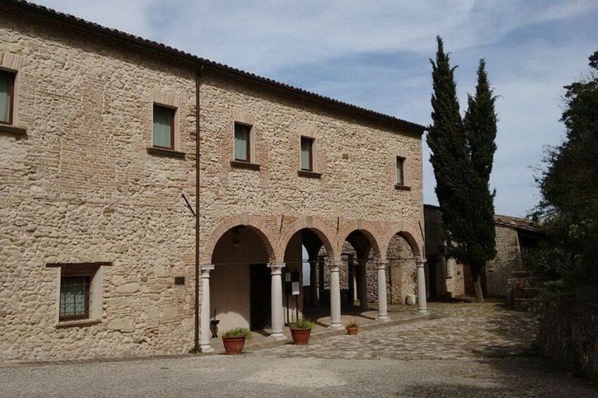 A stone building with arched doorways and columns, surrounded by potted plants and trees. 3