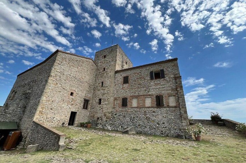 A stone castle with a tower, a grassy courtyard, and a clear blue sky with clouds. 1