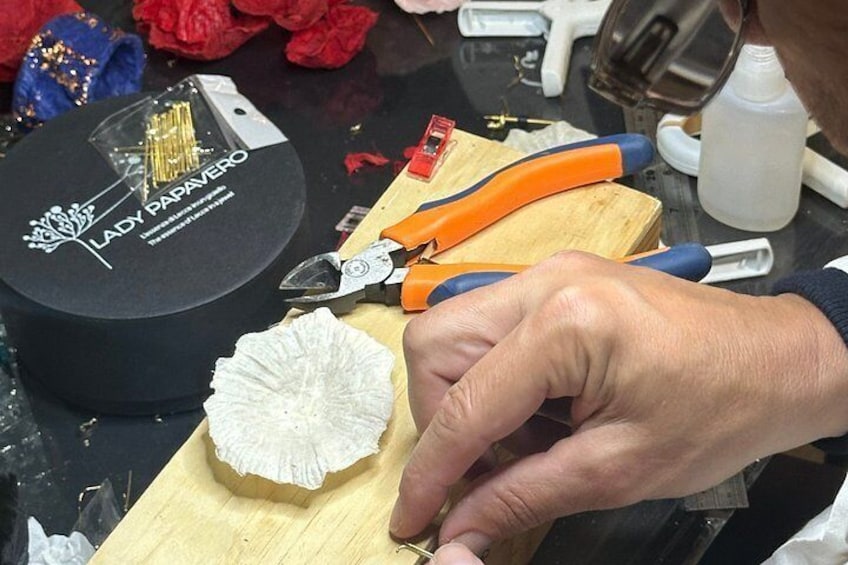 A person using pliers to work on a piece of paper on a wooden board. 4