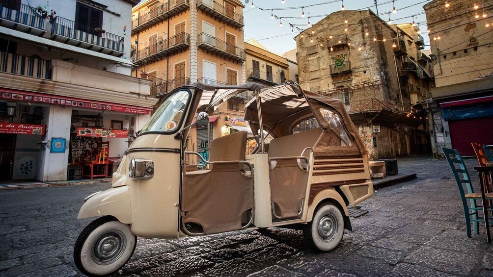 A vintage tuk-tuk parked on a cobblestone street with buildings and string lights in the background. 5