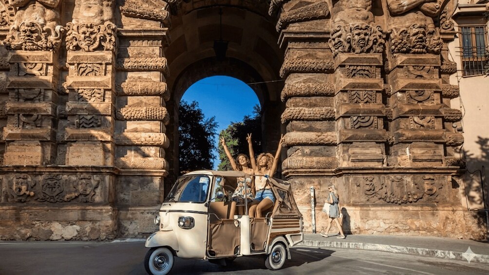 A vintage car parked in front of an ornate stone archway. 3