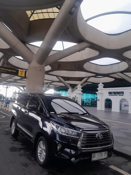 A black SUV parked under a modern architectural structure with a sign indicating 'Departure' and 'SOS Help.' 4
