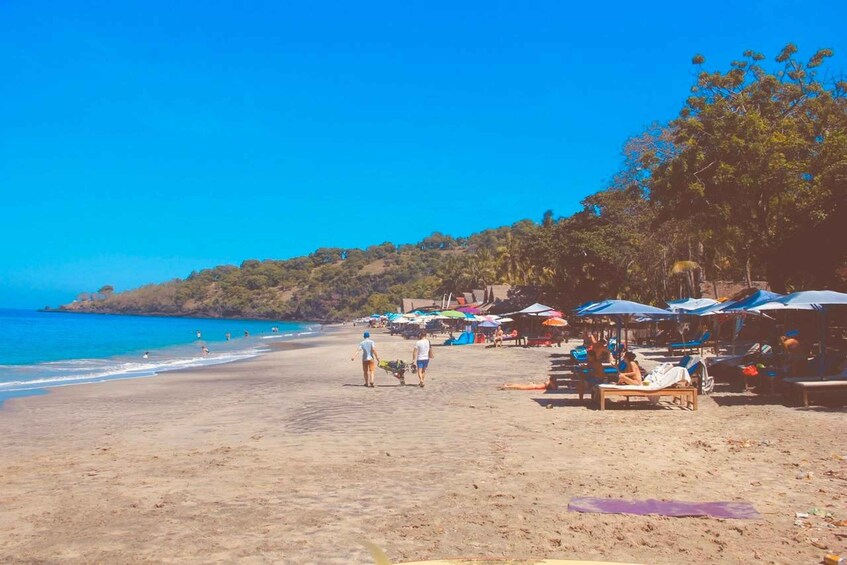 A beach with people sunbathing, umbrellas, and a clear blue sky. 3