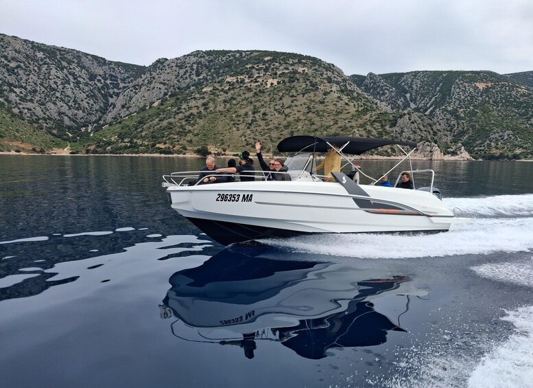 A white motorboat with the number 296353 MA on its side, moving on a calm lake with reflections, surrounded by green hills. 1