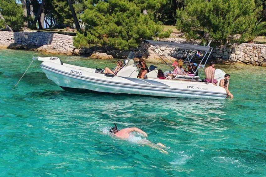 Ein Boot mit Personen, ein Schwimmer im Wasser und eine felsige Küste mit Bäumen. 3