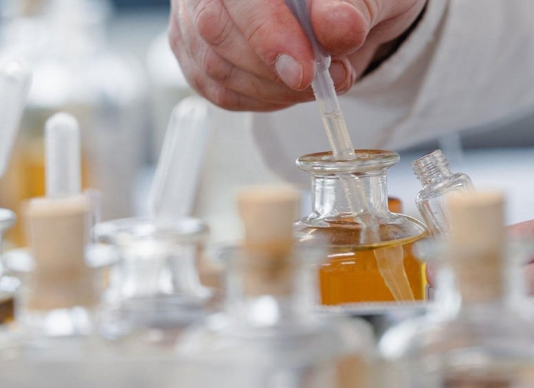 A person handling a pipette in a laboratory setting with multiple glass containers. 1