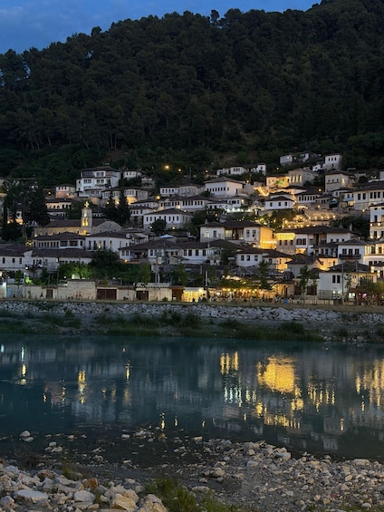 A hillside village with buildings reflecting on a calm river. 1