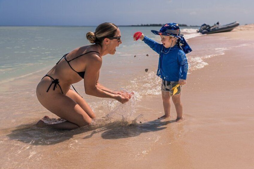 A woman in a bikini and a child in a blue outfit playing with water on a sandy beach. 4