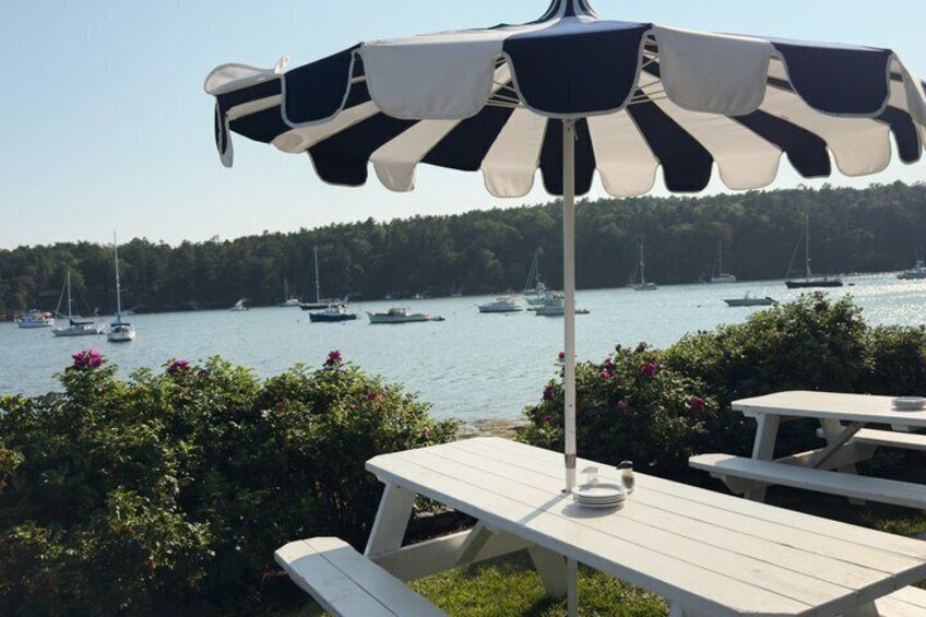 A lakeside picnic area with tables and an umbrella, overlooking a calm lake with sailboats. 5