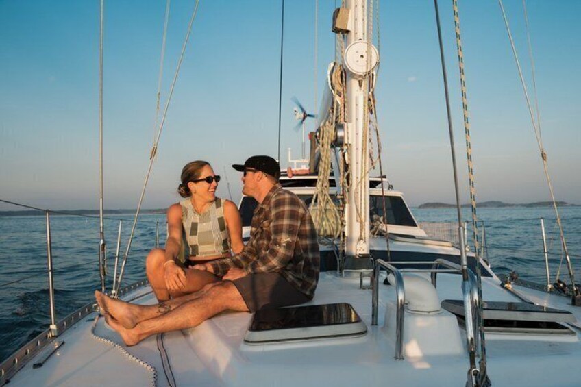 A couple sitting on a sailboat with the ocean in the background. 1