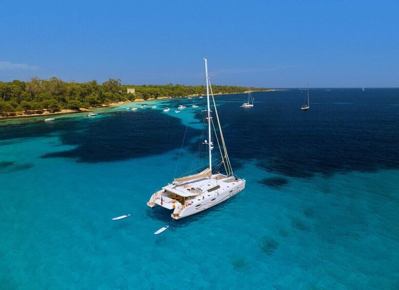 A white sailboat anchored in clear turquoise waters with a backdrop of a forested coastline and other boats in the distance. 3