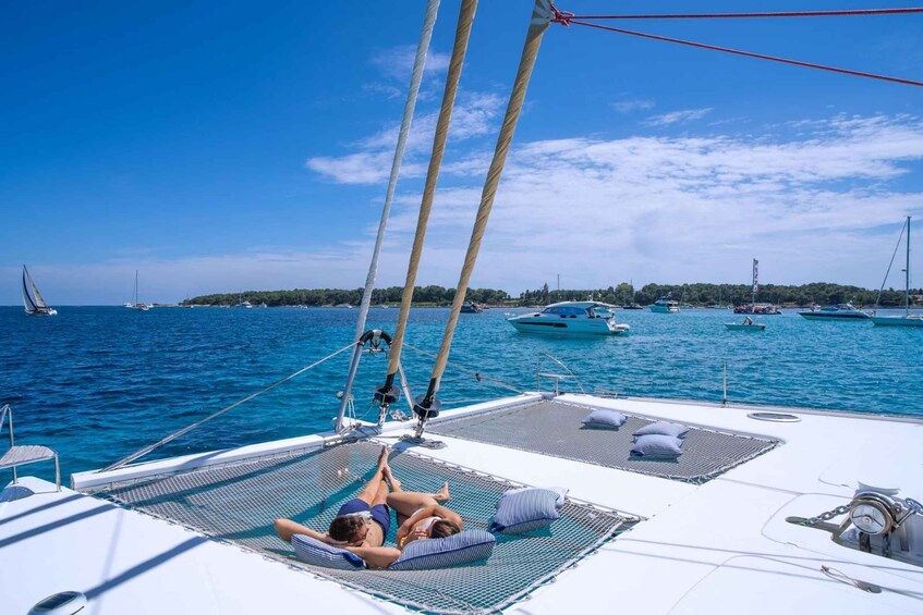A sailboat with two people relaxing on a sunbed, surrounded by calm blue waters and other boats. 2