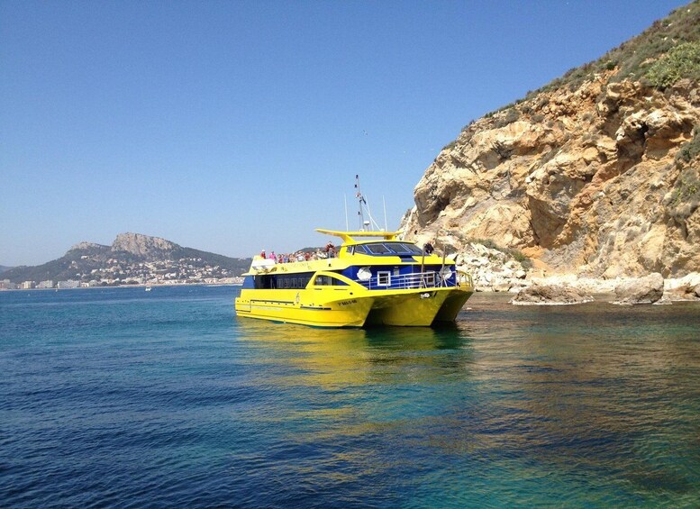 A yellow boat with passengers on a calm sea, rocky coastline, and a distant hill. 2