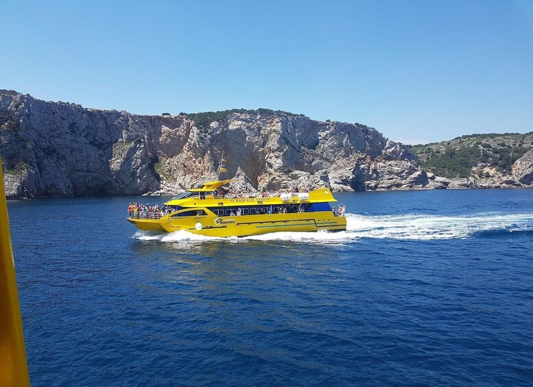 A yellow boat with passengers, moving through a body of water with rocky cliffs in the background. 5